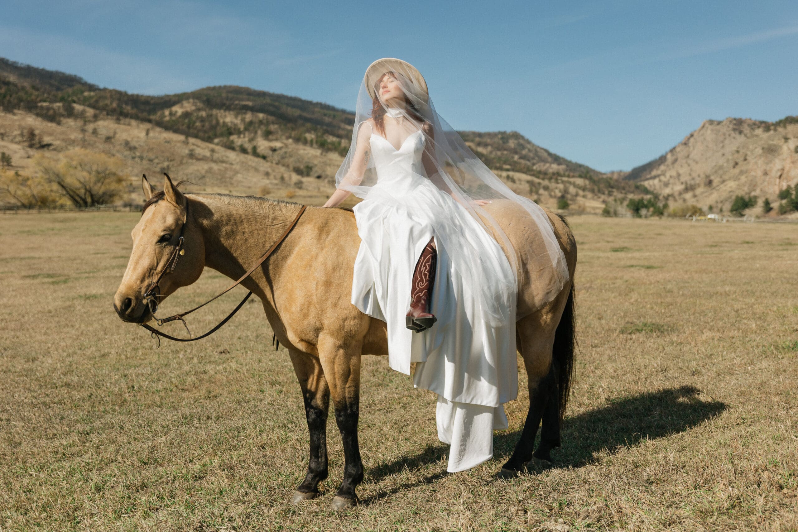 Western bride sitting side saddle with veil over her face at a ranch elopement in Colorado.